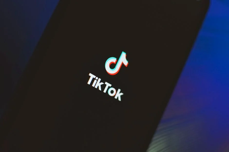 Close-up of a smartphone displaying a blurred image, placed on a desk beside a laptop.